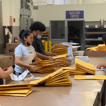 A group of people packing envelopes in a warehouse.